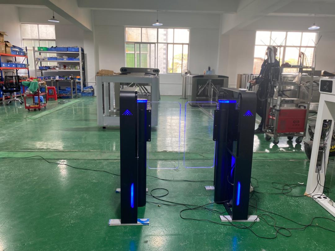 Ժամանակակից ավտոմատ տուրնիկետ թափանցիկ ապակե փեղկերով, սև-մոխրագույն կորպուսով և կանաչ LED լուսային ցուցիչով՝ մուտքի վերահսկման համակարգի համար